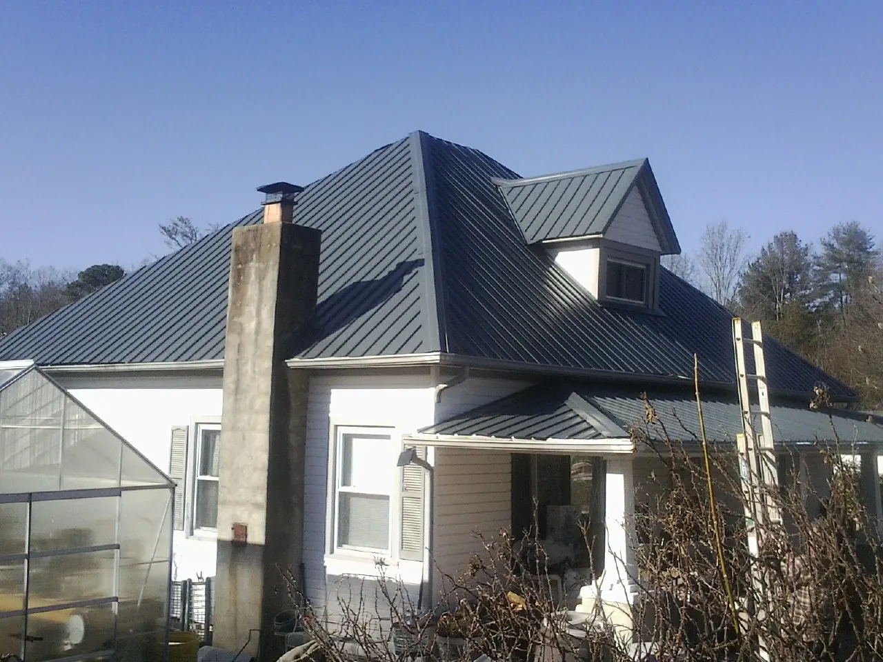 Dark blue standing seam metal roof on a white farmhouse with dormer — Slate & Tile Roof Repair by Roofing Brothers in Buchtel