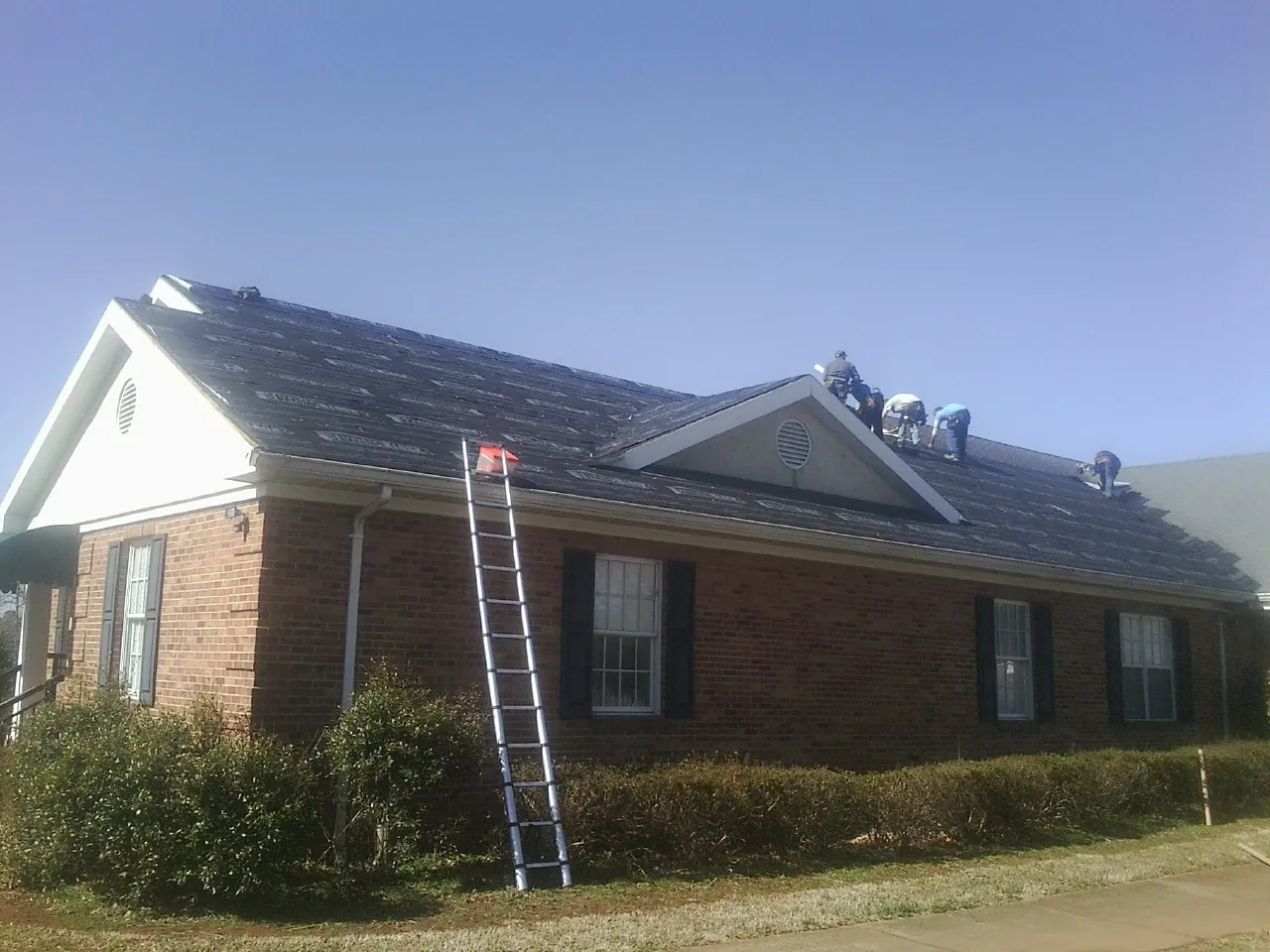 Crew tearing shingles off a brick ranch roof with a ladder set — Emergency Roof Repair work by our crew in Buchtel