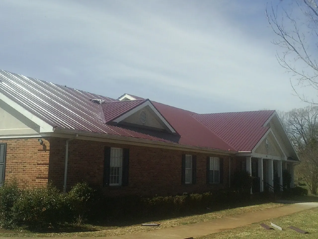 Red metal roof with gabled entries on a long brick building, from a Hail Damage Roof Repair job in Buchtel
