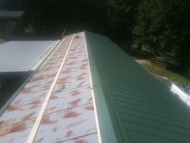 Old rusted panels beside newly installed green metal roofing — Wind Damage Roof Repair by Roofing Brothers in Buchtel