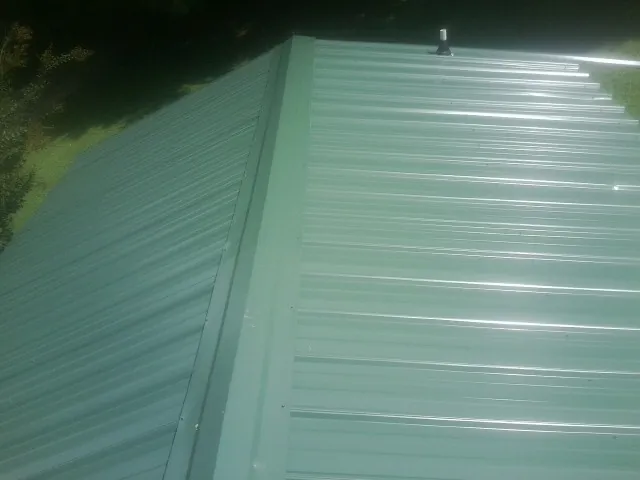 New green metal panels meeting at the ridge of a roof — Flat Roof Repair work by our crew in Buchtel