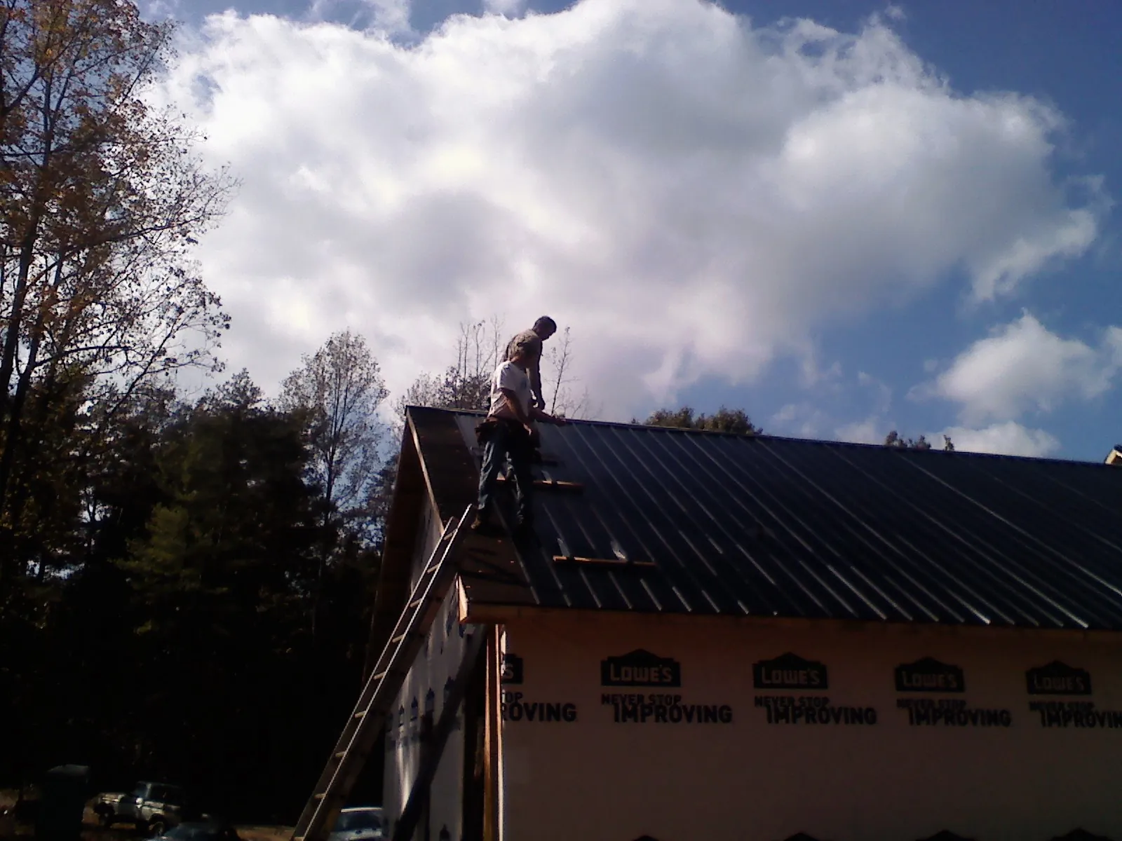 Roofer fastening dark metal panels high against a cloudy sky, from a Roof Inspection job in Buchtel