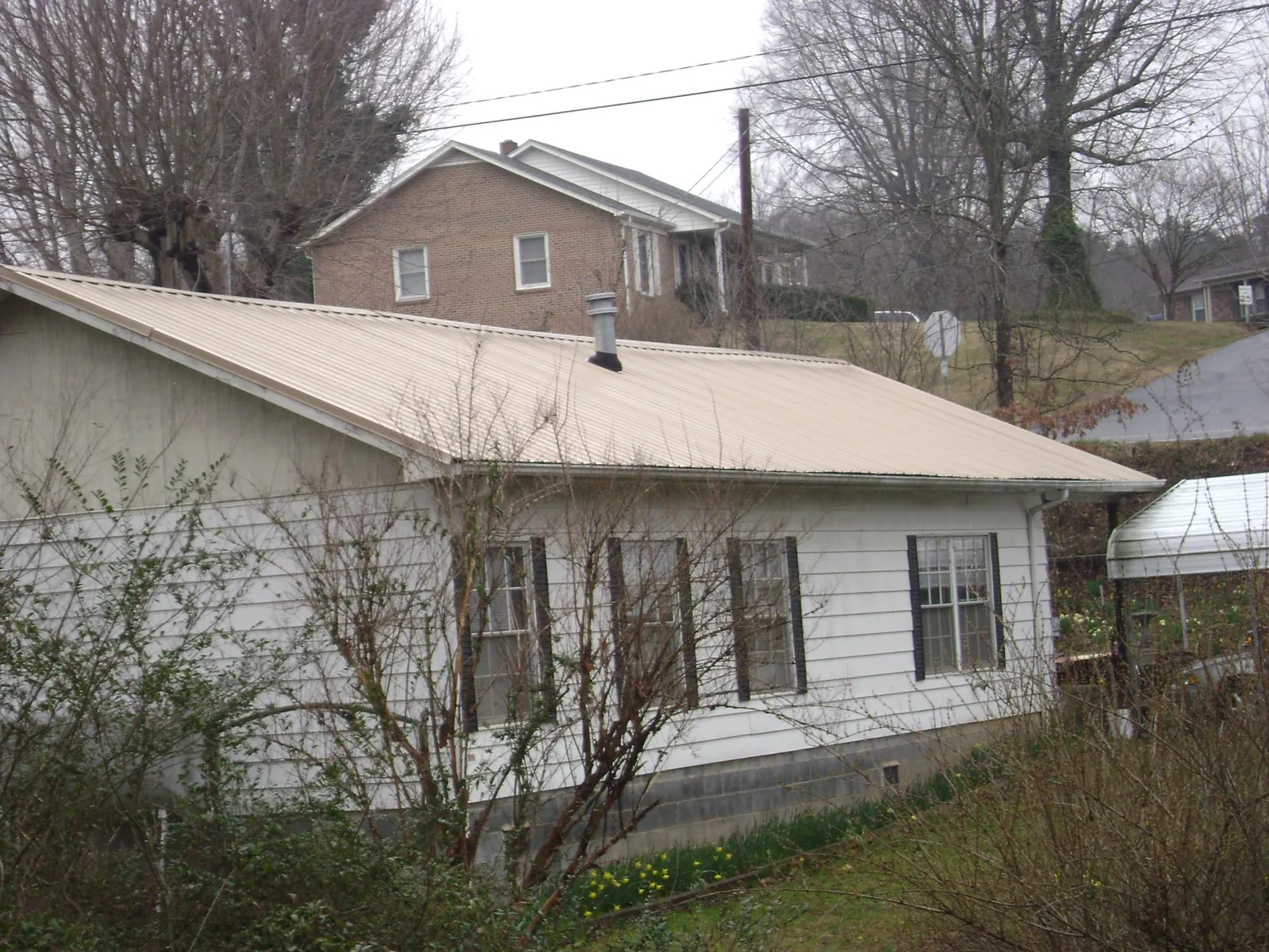 Tan metal roof on a white sided house set into a hillside — Commercial Roofing by Roofing Brothers in Buchtel