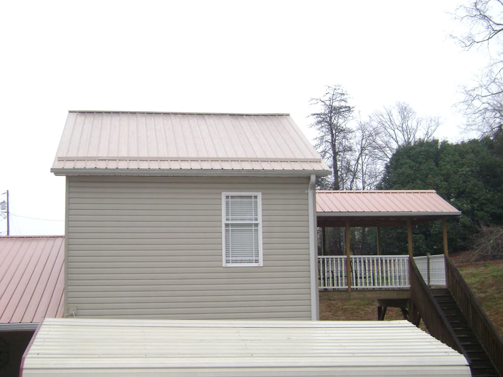 Tan metal roofs on a two story addition and attached porch, from a Roof Replacement job in Buchtel